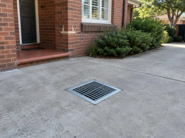 Concrete driveway with a metal drain grate beside a brick home in Beecroft