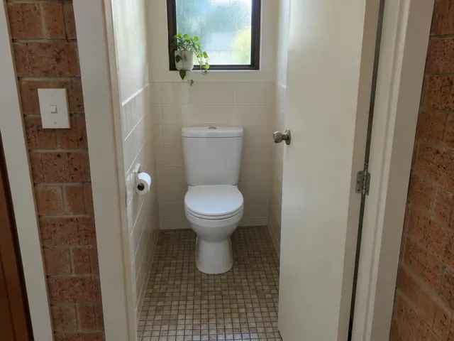 Clean white toilet in a tiled small bathroom with brick doorway and frosted window in Carlingford