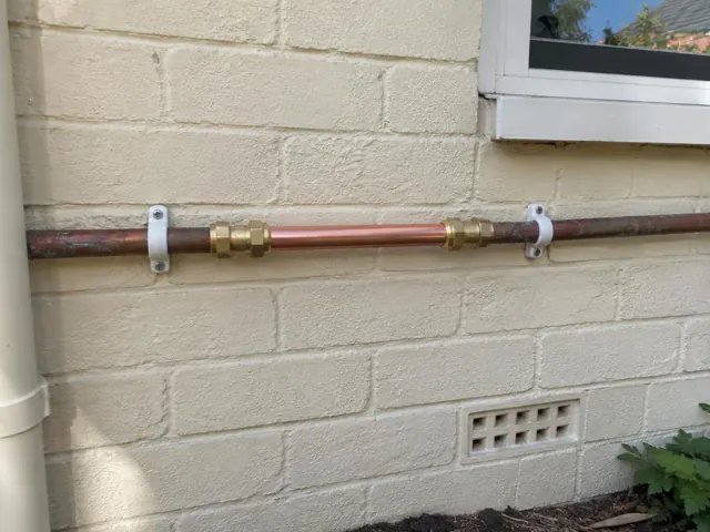 Repaired copper water pipe on a painted brick exterior wall beneath a window in Beecroft