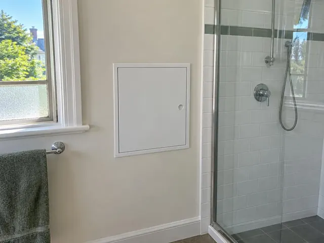 Bathroom wall with a small access panel beside a tiled shower and window in Normanhurst